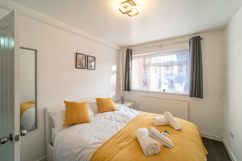 Bright bedroom with double bed, yellow bedding, white pillows, and large window with grey curtains