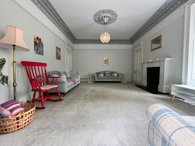 Spacious living room with red chair, sofa, fireplace, pendant light and period ceiling details
