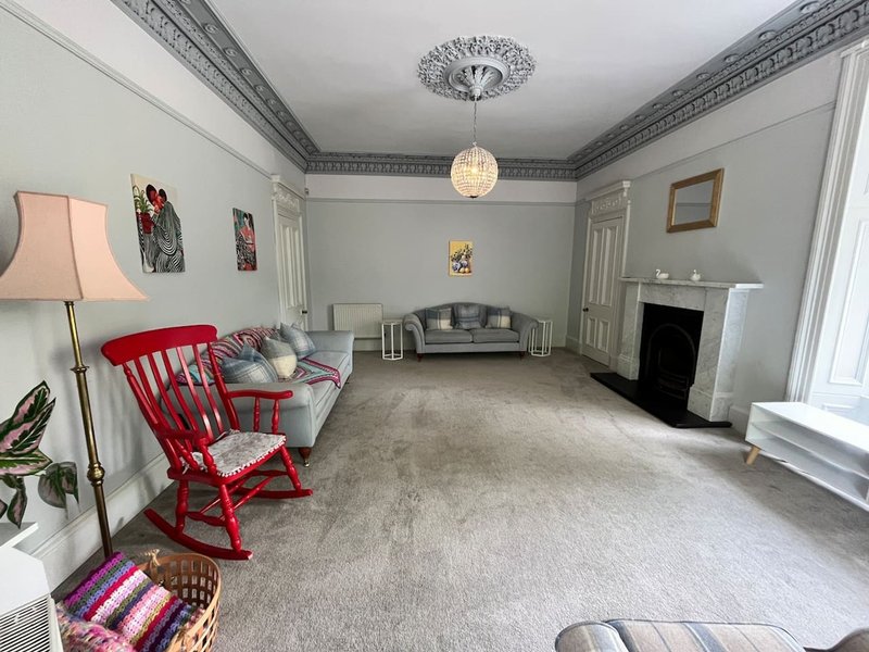 Spacious living room with red rocking chair, gray sofa, fireplace, and decorative ceiling details