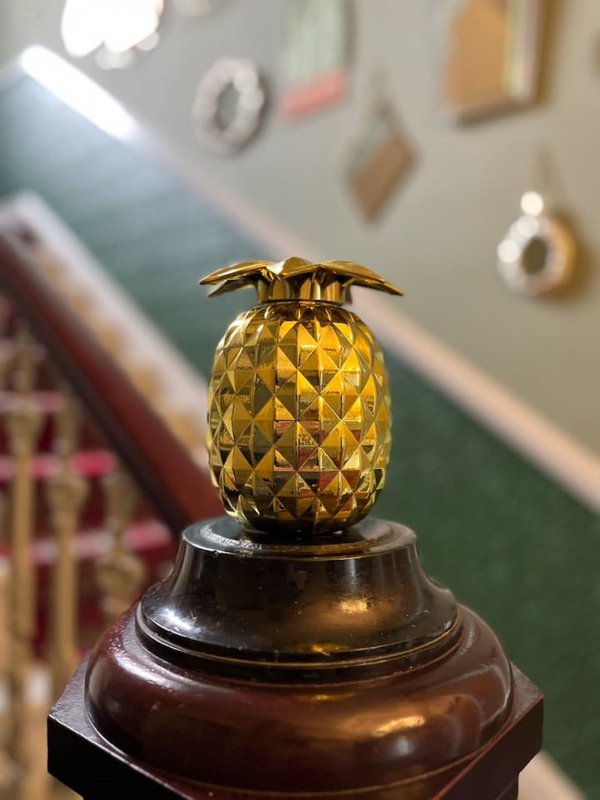 Gold pineapple decorative ornament on wooden stand, interior room with wall decor