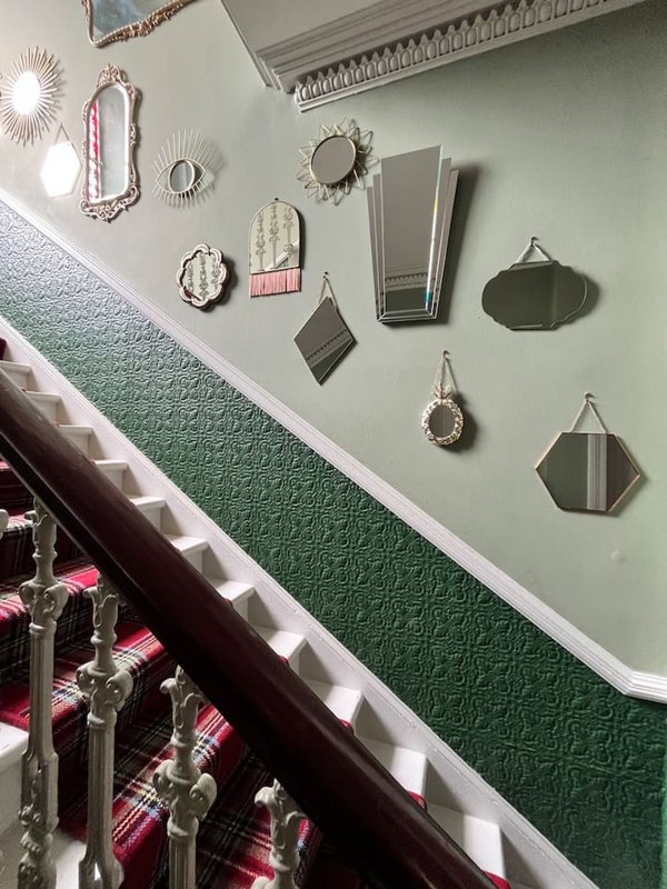 Staircase with green textured wallpaper and decorative mirrors on pale wall
