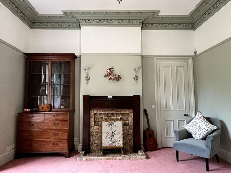 Period living room with fireplace, wooden cabinet, armchair and decorative ceiling cornicing