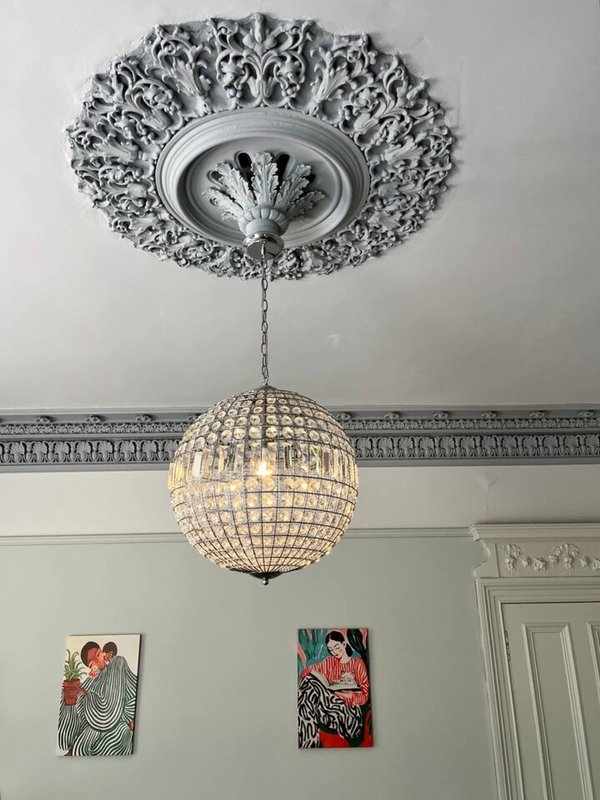 Ornate ceiling rose with crystal pendant light fixture and framed artwork on walls
