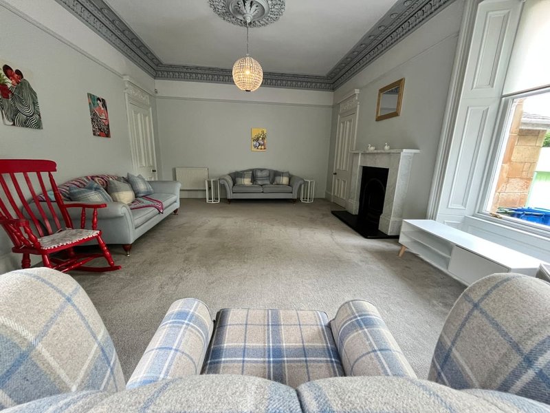Spacious living room with fireplace, sofa, red armchair, pendant light and large windows