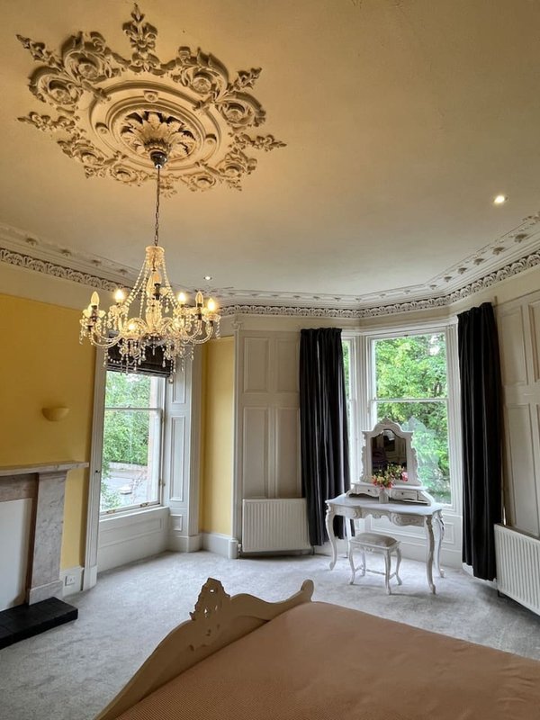 Elegant bedroom with ornate ceiling rose, chandelier, fireplace and large windows