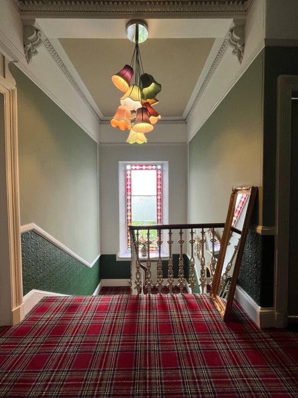 Hallway with staircase, colourful pendant light, tartan carpet, and window at end