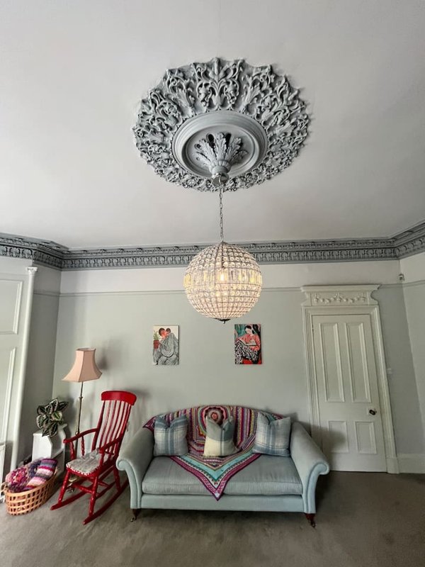 Living room with ornate ceiling rose, crystal pendant lamp, gray sofa and red rocking chair