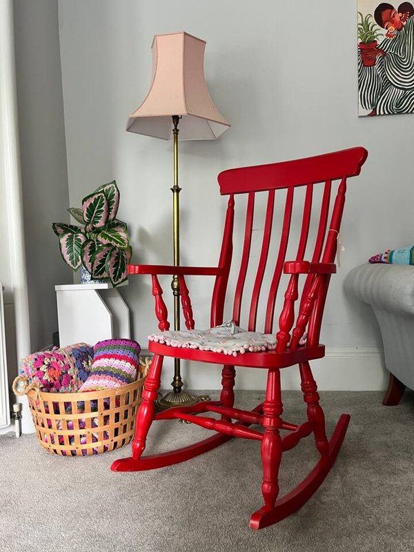 Red wooden rocking chair with cushion, floor lamp, potted plant and decorative basket in living room