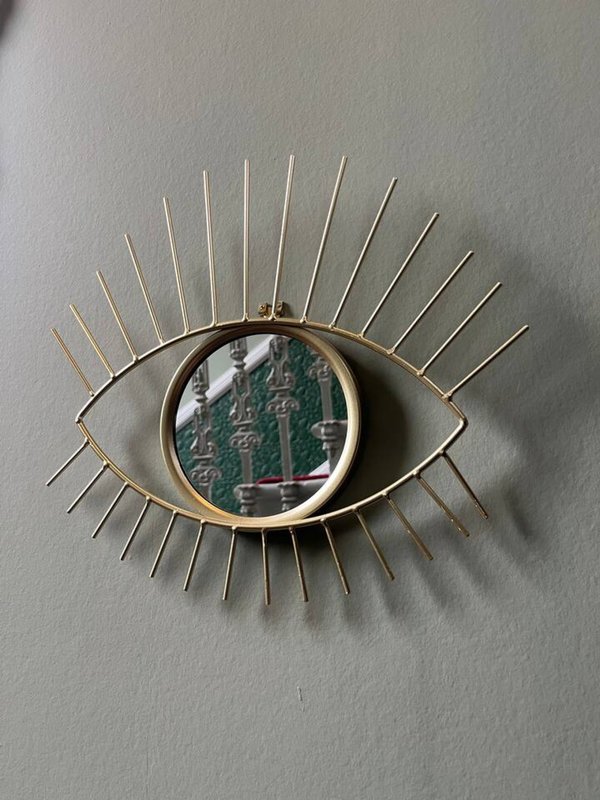 Decorative brass eye-shaped wall mirror with radiating spokes and circular center panel