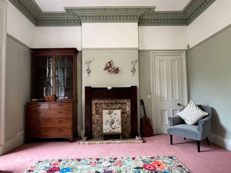 Period living room with decorative fireplace, wooden furniture, pink carpet and ornate ceiling