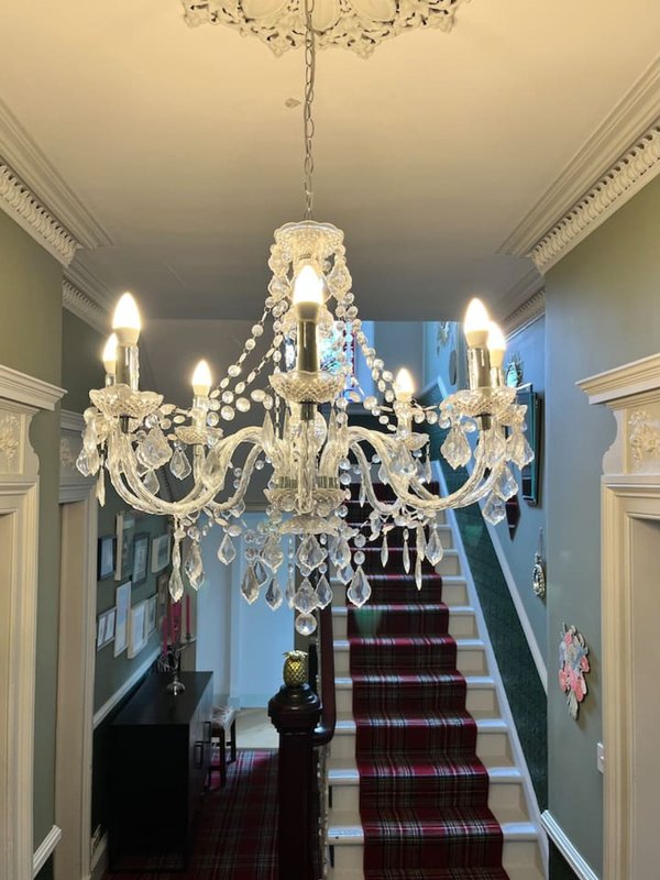 Hallway with ornate crystal chandelier, carpeted staircase, and decorative cornicing