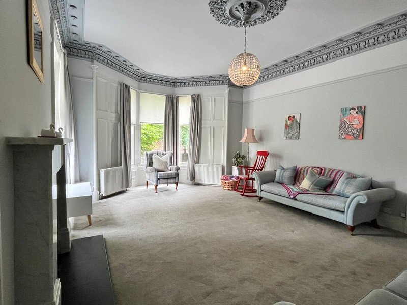 Spacious period living room with corniced ceiling, fireplace, sofa, and bay windows overlooking garden
