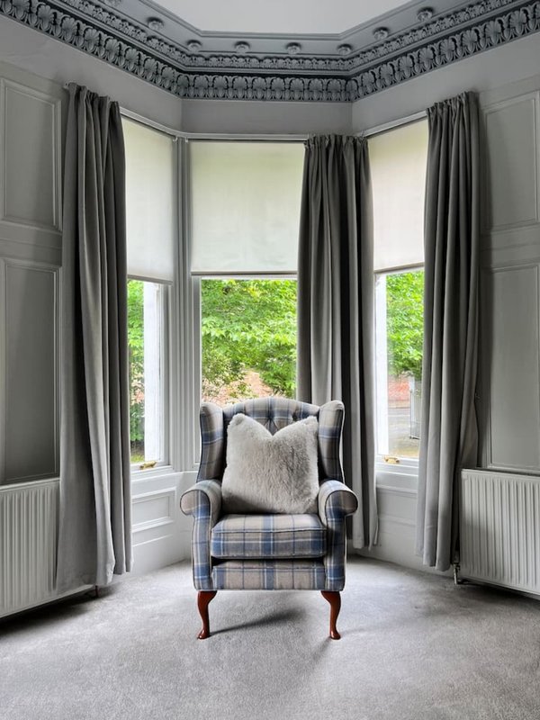 Bay window seating area with upholstered armchair, cushions, curtains and garden view