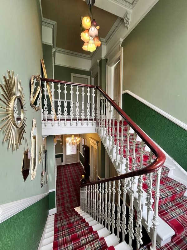 Staircase with white railings, green and white walls, red tartan carpet, pendant lighting