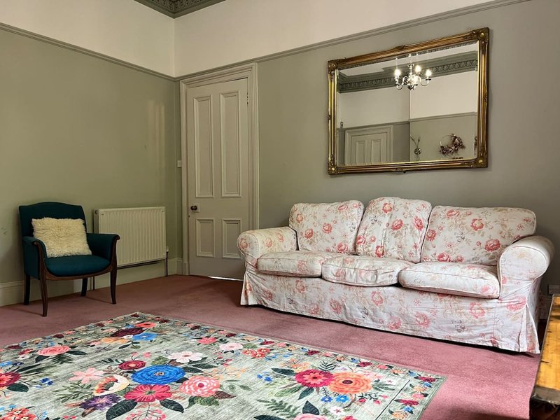 Living room with floral sofa, armchair, decorative rug, mirror and pale green walls
