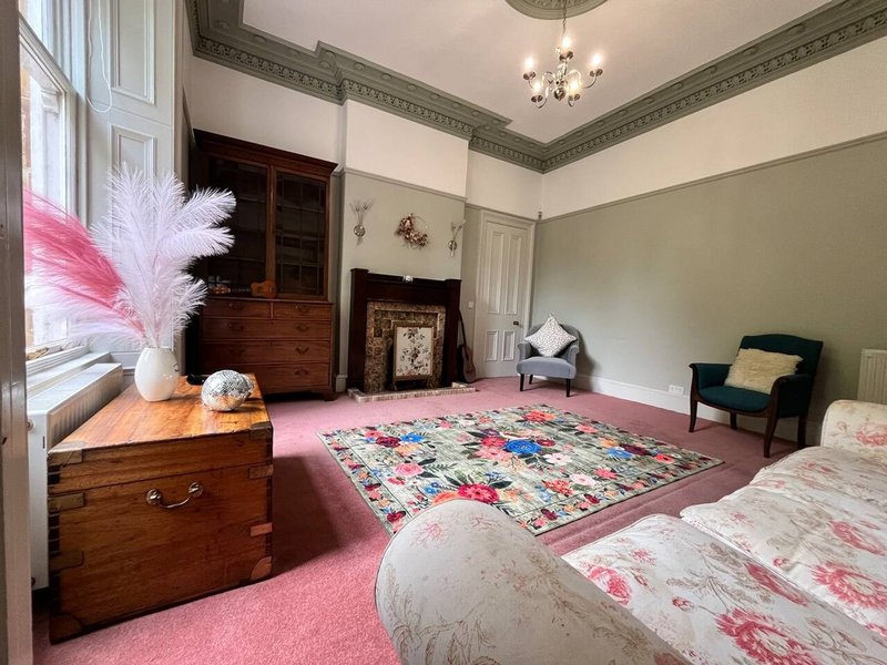 Spacious bedroom with twin beds, wooden chest, patterned rug, pampas grass arrangement and period features