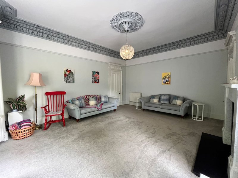 Spacious living room with ornate ceiling, two sofas, red chair, lamps and framed artwork