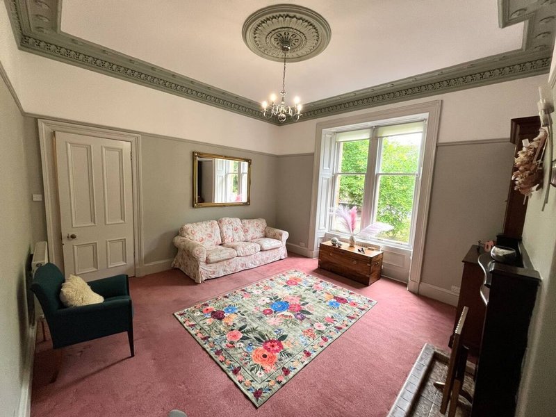 Bright living room with pink patterned rug, floral sofa, black armchair and ornate ceiling