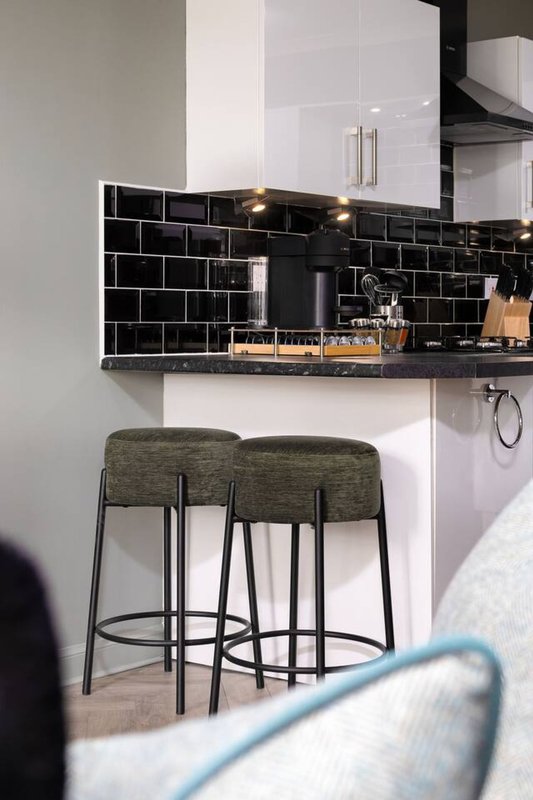 Modern kitchen with black subway tile backsplash, white cabinetry, and two upholstered bar stools