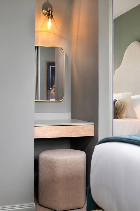 Modern bedroom vanity with mirror, wall sconce lighting, and upholstered stool