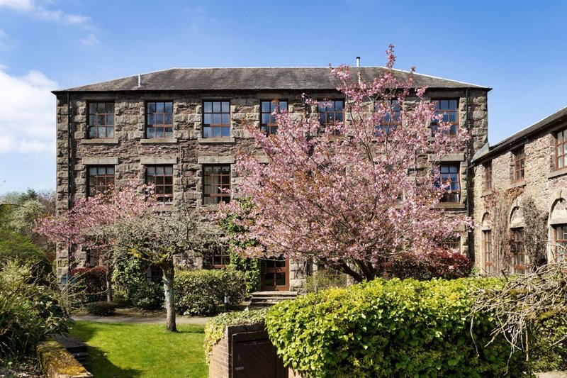 Stone country house with blooming pink magnolia tree and manicured garden grounds