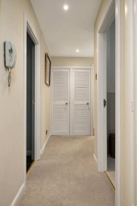 Hallway with beige carpet, white louvered closet doors and recessed ceiling lights