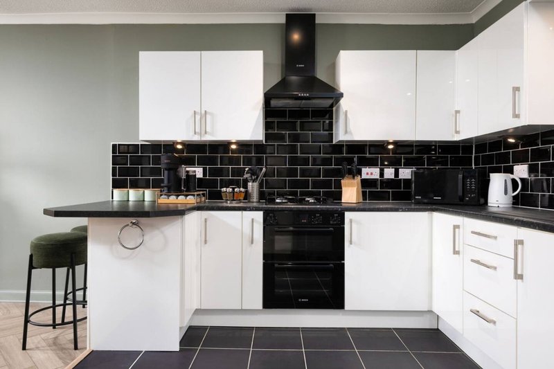 Modern kitchen with white cabinetry, black tile backsplash, black range cooker and bar stool