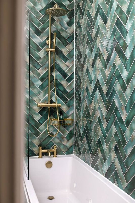 Modern bathroom shower with green herringbone tile wall and brass rainfall showerhead