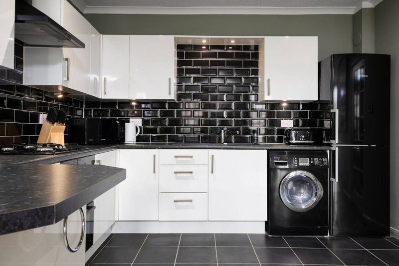 Modern kitchen with white cabinetry, black subway tile backsplash, dark countertops and black appliances