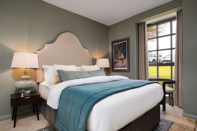 Modern bedroom with upholstered headboard, blue bedding, table lamps, and large window with autumn views