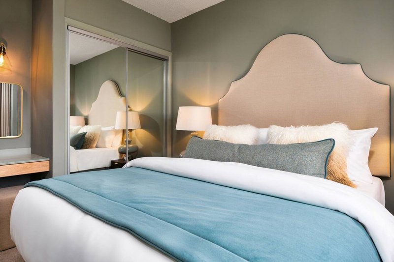 Modern bedroom with upholstered headboard, blue throw blanket, white bedding and mirrored wardrobe