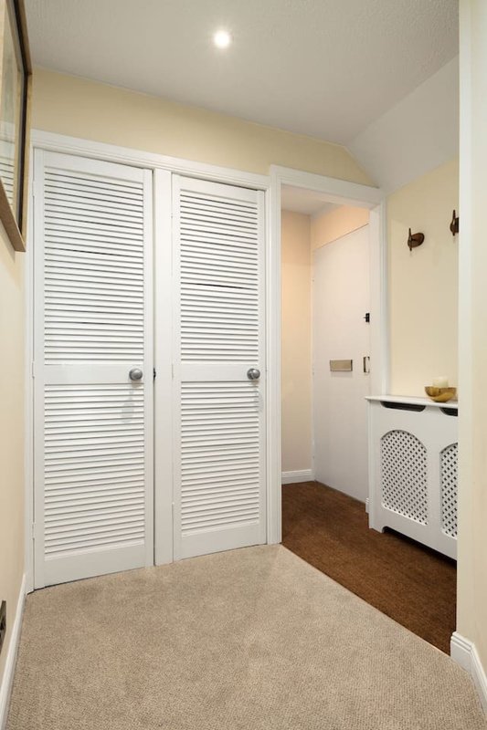 Hallway with white louvered closet doors, carpet flooring, and white radiator cover