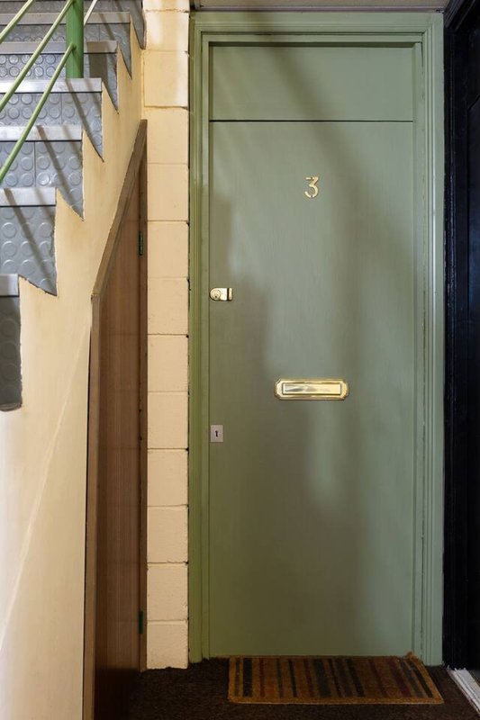 Green front door entrance with cream stone surround and brown doormat