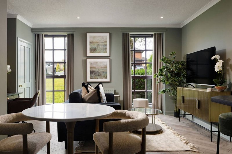 Modern living room with round white table, upholstered chairs, TV, framed artwork and garden views