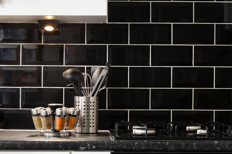 Kitchen countertop with black subway tile backsplash, utensil holder, and decorative glasses