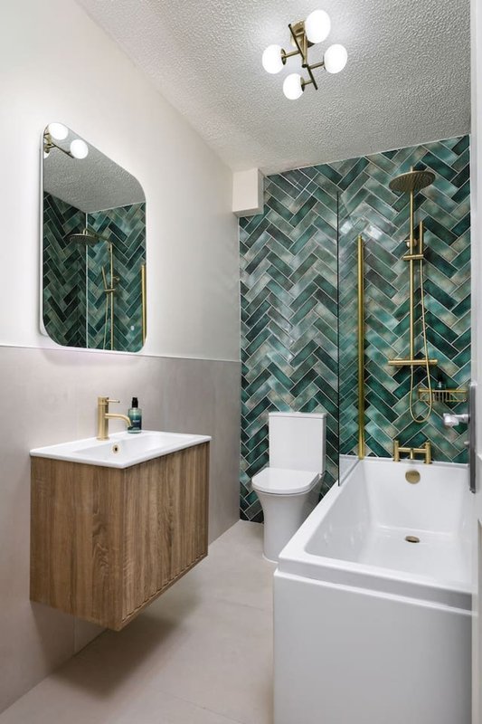 Modern bathroom with green herringbone tile wall, wooden vanity, white sink and toilet