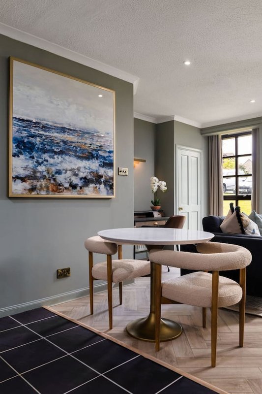 Modern dining area with round white table, wooden chairs, framed blue artwork and window view