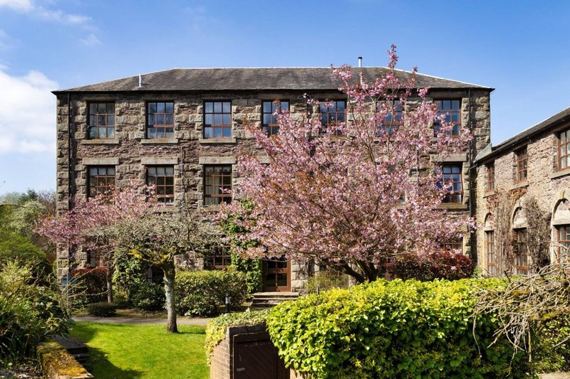 Stone property exterior with blooming cherry trees, manicured garden and green lawn