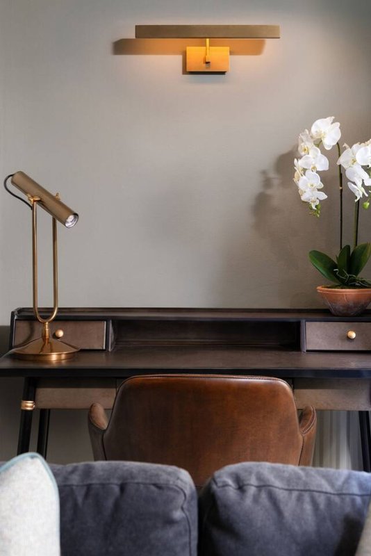 Modern desk with wooden chair, desk lamp, potted orchid plant, and wall-mounted light fixture