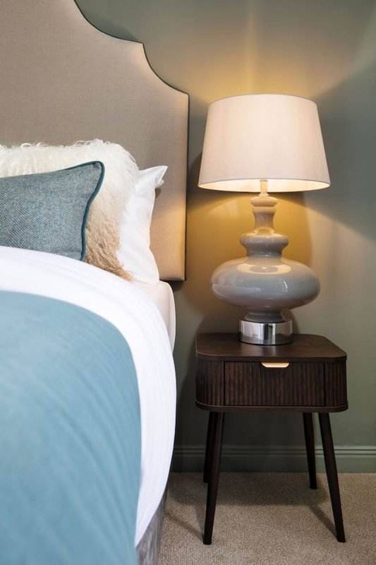 Bedroom corner with double bed, decorative pillows, wooden nightstand and table lamp