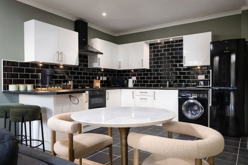 Modern kitchen with white cabinets, black subway tile backsplash, and dining table with upholstered chairs