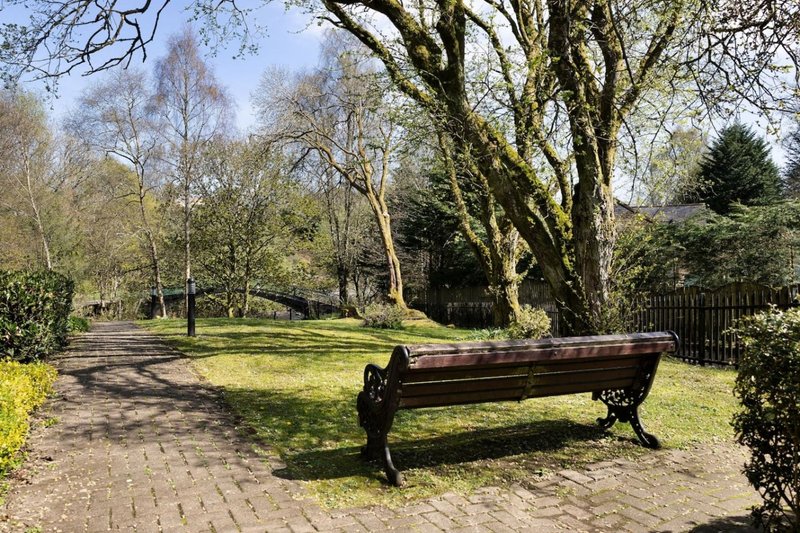 Park grounds with large bare trees, wooden bench on brick pathway, and manicured lawn
