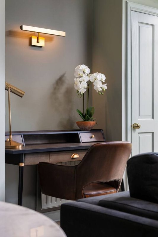 Modern bedroom corner with wooden desk, brown leather chair, white orchid plant, and wall sconce lighting