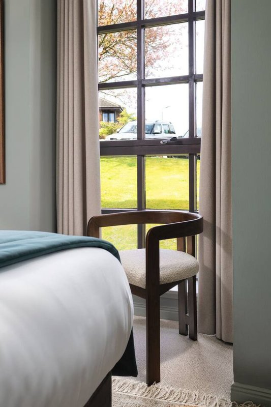 Bedroom corner with double bed, wooden chair, window with garden view and curtains