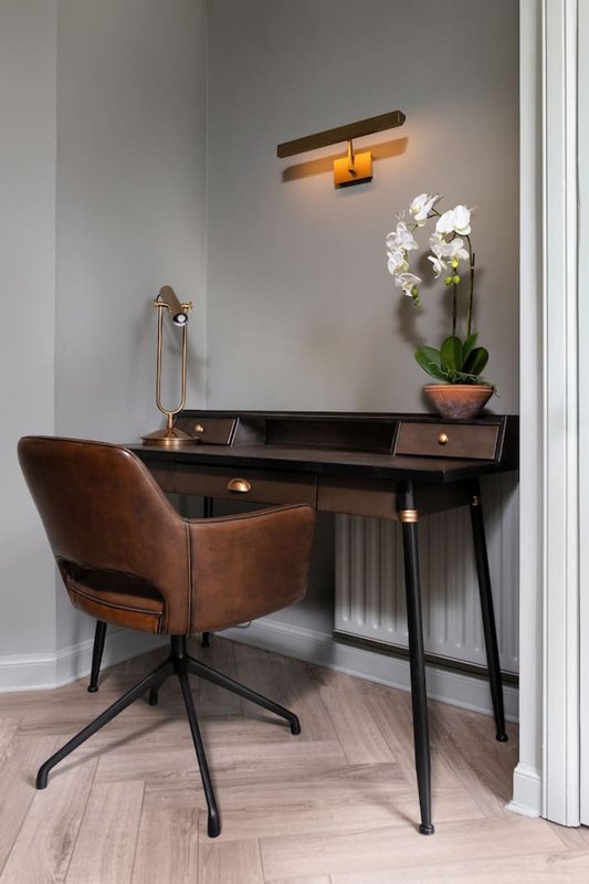 Modern desk with brown leather chair, potted white orchid, and wall-mounted wooden light fixture