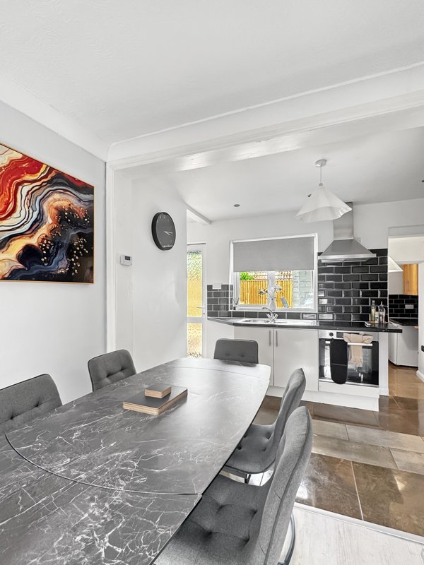 Open-plan dining and kitchen area with marble table, grey chairs, and modern black tile backsplash