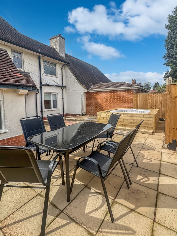 Patio area with dining table, chairs, and brick house exterior with garden