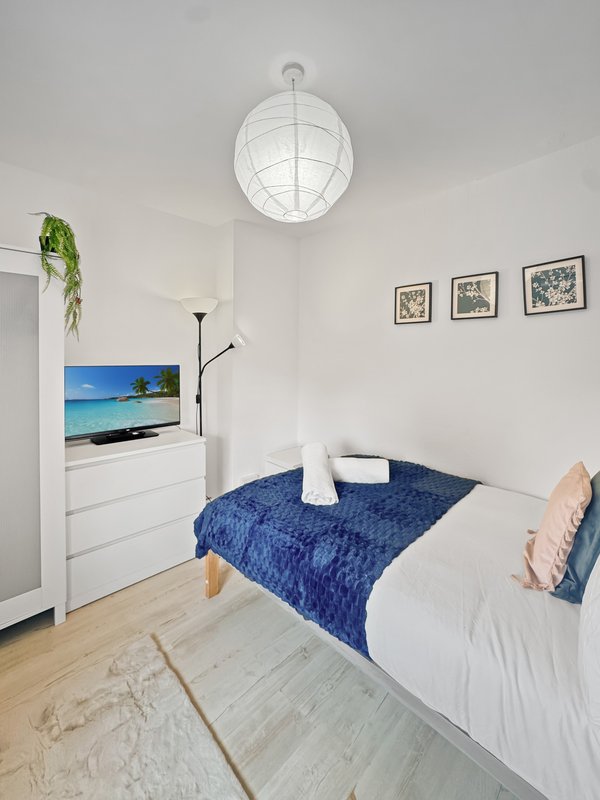 Compact bedroom with single bed, blue throw blanket, white pendant light and wall-mounted TV