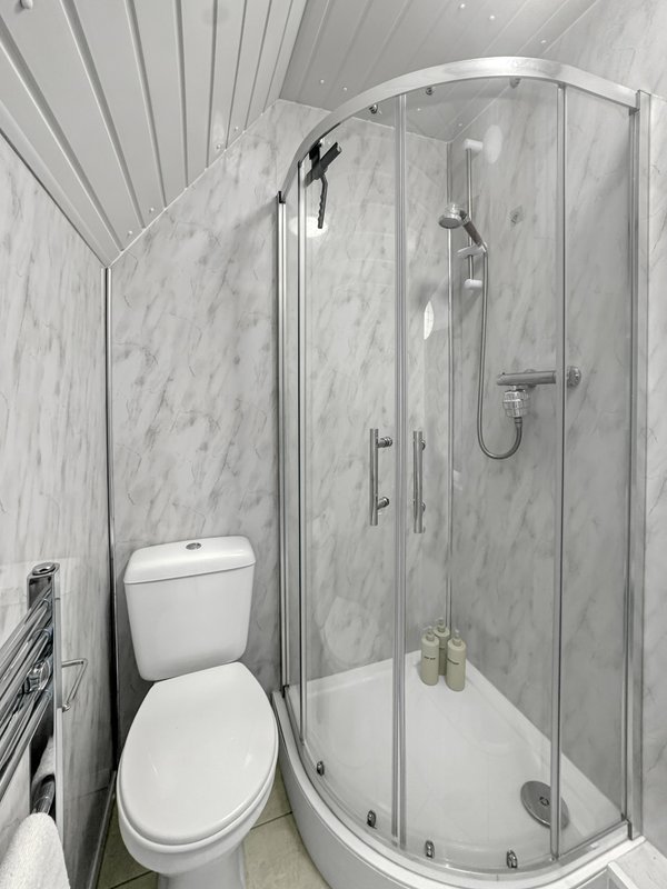 Modern bathroom with marble-effect tiles, corner shower enclosure, white toilet and heated towel rail