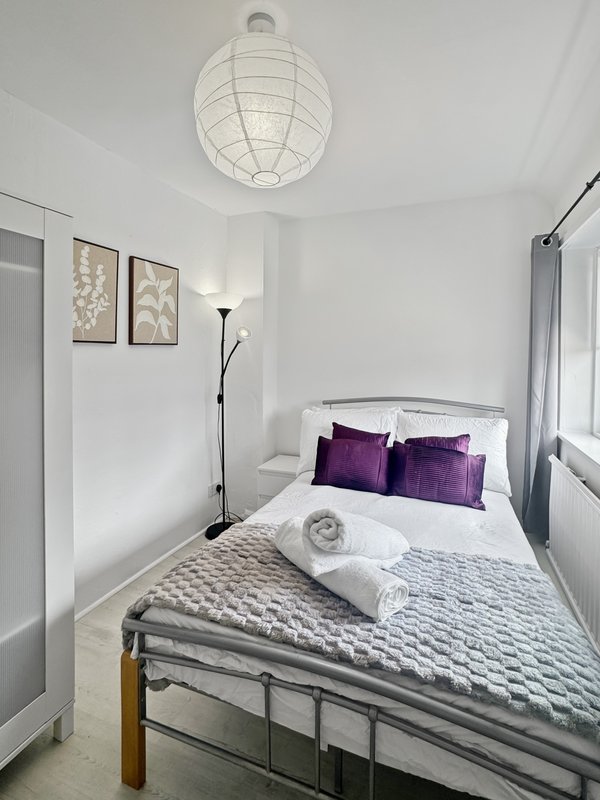 Bright bedroom with double bed, purple pillows, pendant light, and framed wall art